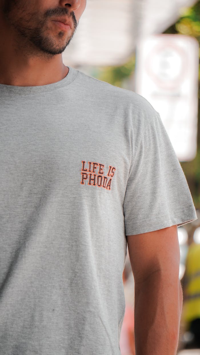 Close-up of a man in a gray crew neck t-shirt with text detail outdoors.