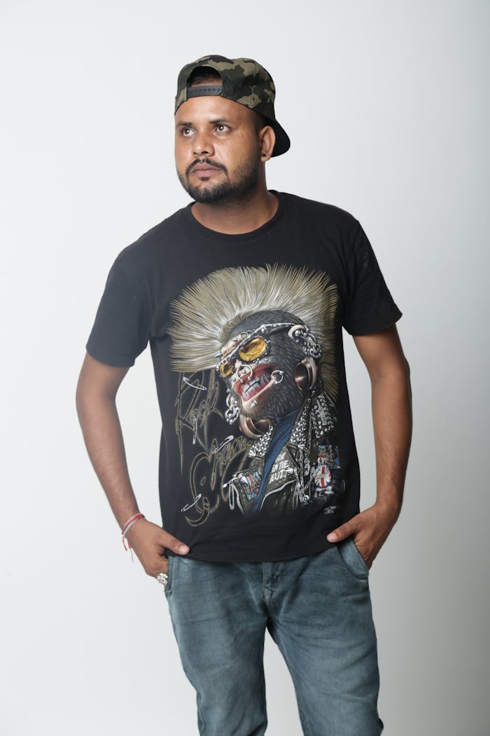 Studio portrait of a young man in a graphic T-shirt and cap, posing confidently.