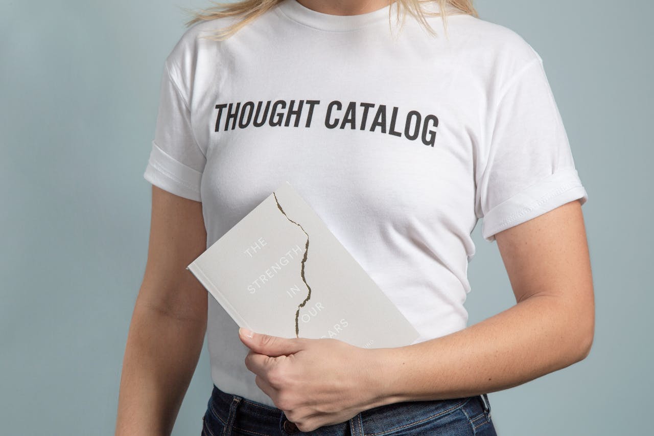 A woman wearing a white t-shirt holds a book with a cracked cover.