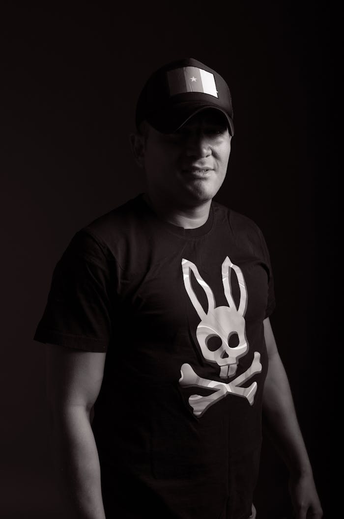 A black and white portrait of a man in a cap and graphic t-shirt, exuding a moody vibe.