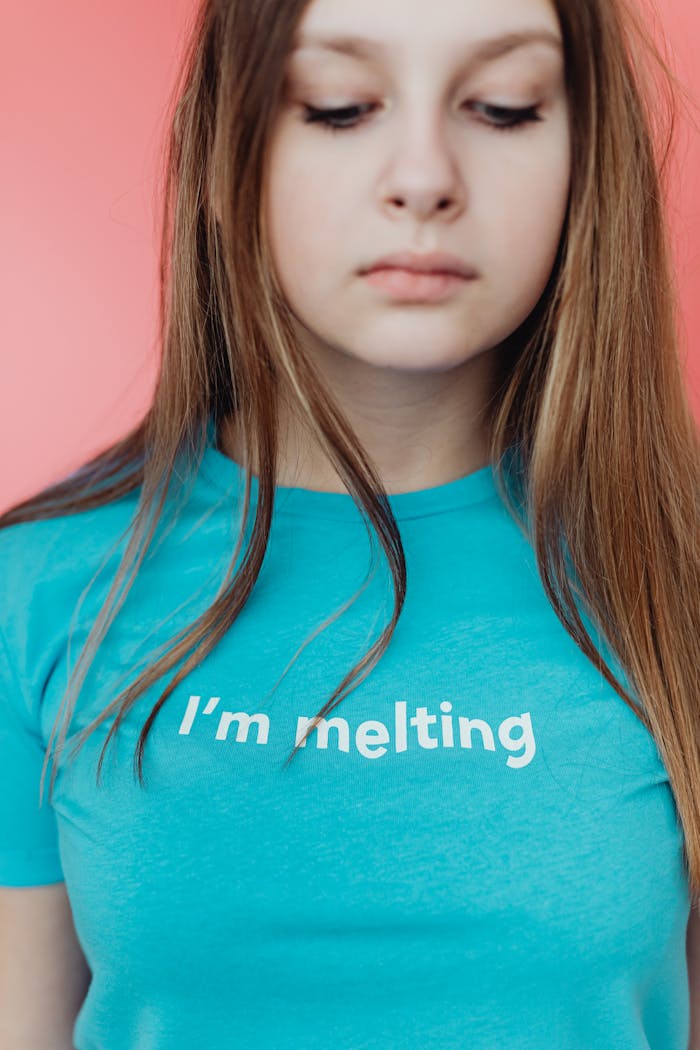 Studio portrait of a teenage girl wearing a blue t-shirt with the phrase 'I'm melting' on a pink background.